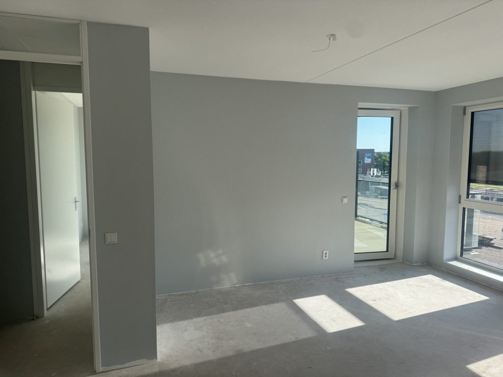 Kamer in een nieuw appartement met lichtgrijze wanden, een betonvloer en een deur naar het balkon
