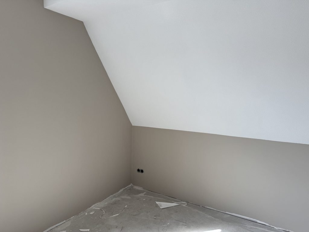 Zolderkamer in een nieuw huis met een schuine wand en strak afgewerkte muren in een zachte tint