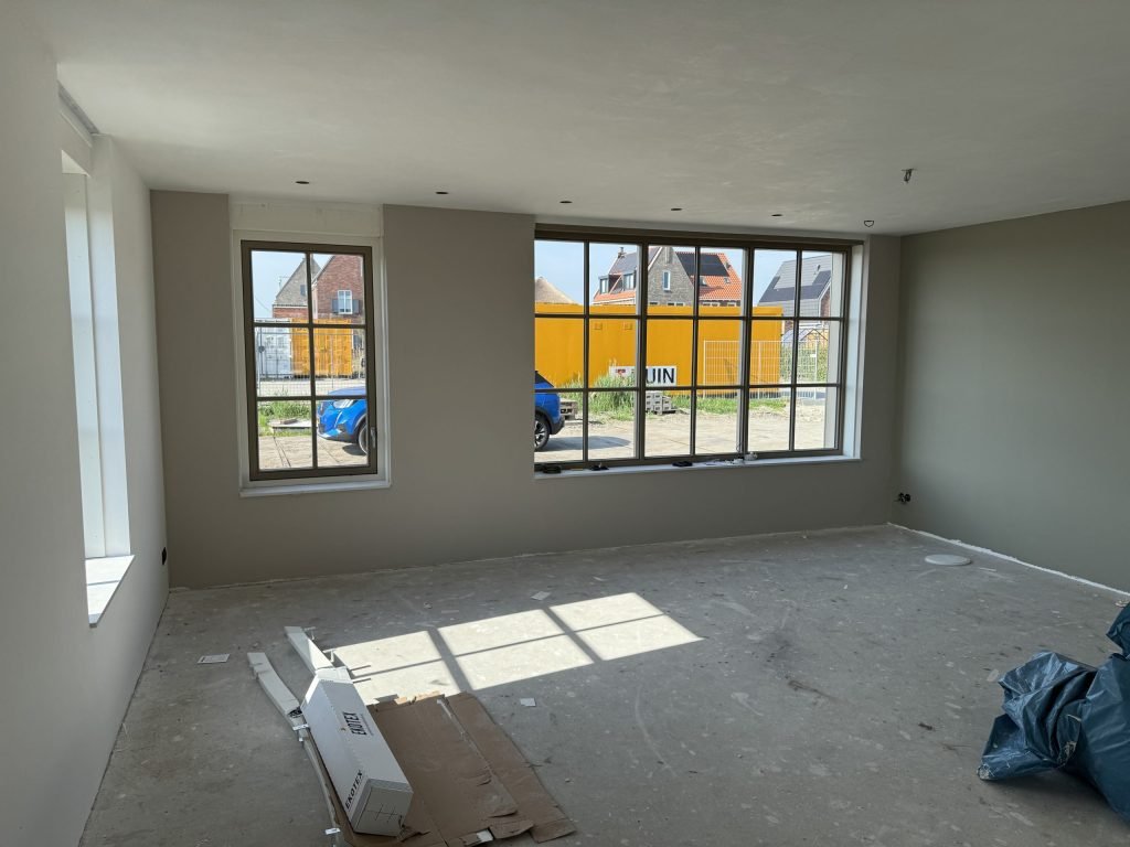 Nieuwe woonkamer met wanden in een warme grijstint, ramen met roeden en een betonvloer