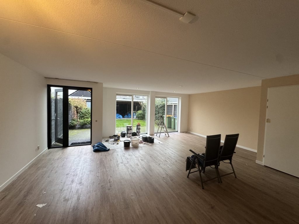 Lege woonkamer in een nieuwe woning met lichte wanden, een houten vloer en verfemmers bij de tuindeuren